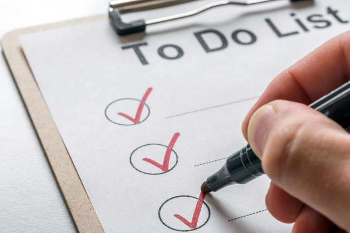 Hand mit Stift, die Haken auf einer To-Do-Liste abhakt.